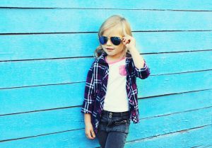 Fashion kid, stylish child wearing a sunglasses and checkered shirt standing over blue background, looking away